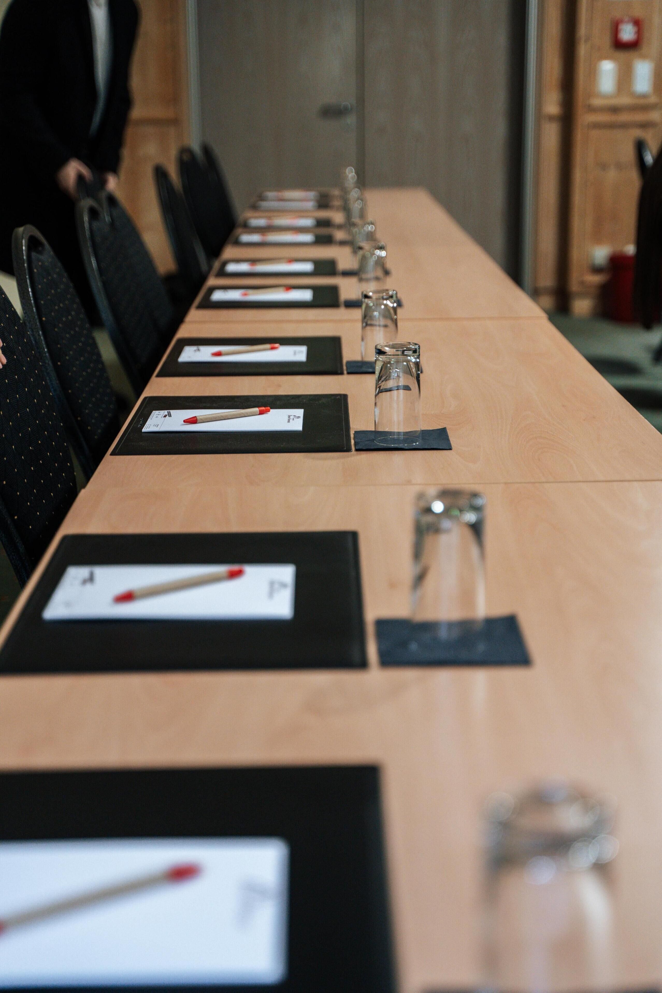 Una mesa de conferencias con tarjetas de identificación y un bolígrafo, ubicada en una sala con sillas y un armario de madera.