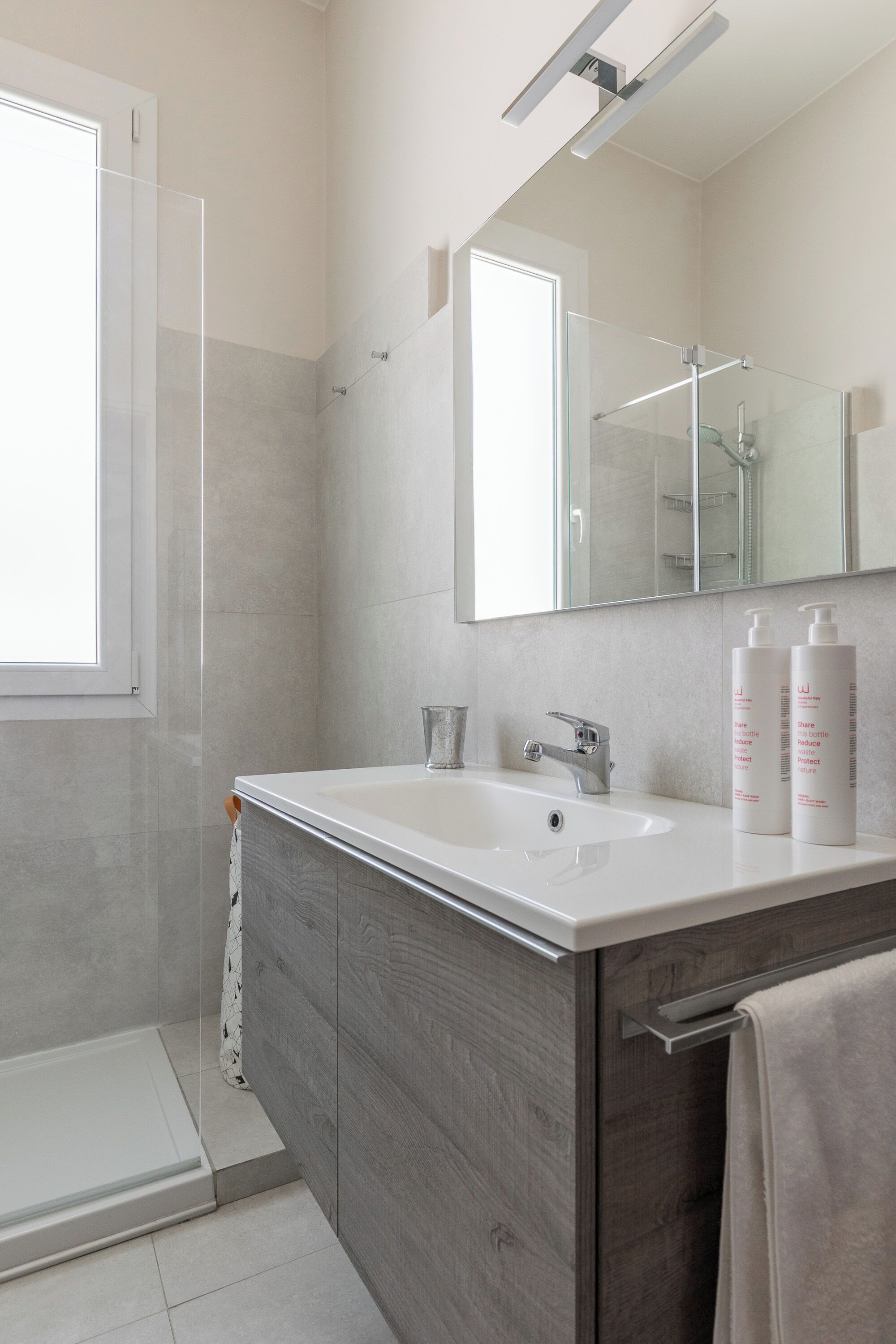 Un baño moderno con un espejo grande, un lavabo blanco y dos botellas de champú.