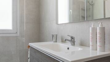 Un baño moderno con un espejo grande, un lavabo blanco y dos botellas de champú.