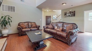 A spacious living room with two leather sofas, a coffee table, and a large potted plant. -  Garden House: A Cozy Retreat (Albuquerque)