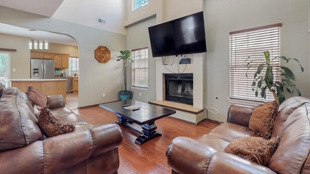 A living room with leather sofas, a coffee table, a flat-screen TV mounted above a fireplace, and a kitchen in the background. -  Garden House: A Cozy Retreat (Albuquerque)