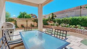 An outdoor patio with a table and chairs, a grill, and a view of a residential area with houses and greenery. -  Garden House: A Cozy Retreat (Albuquerque)