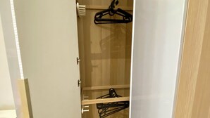 Un petit dressing étroit avec un plancher en bois, une tringle à vêtements et une chaise.