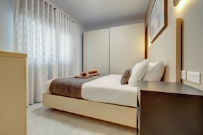 A modern hotel room with a bed, a bedside table, a wall-mounted light, and a curtain with a geometric pattern.