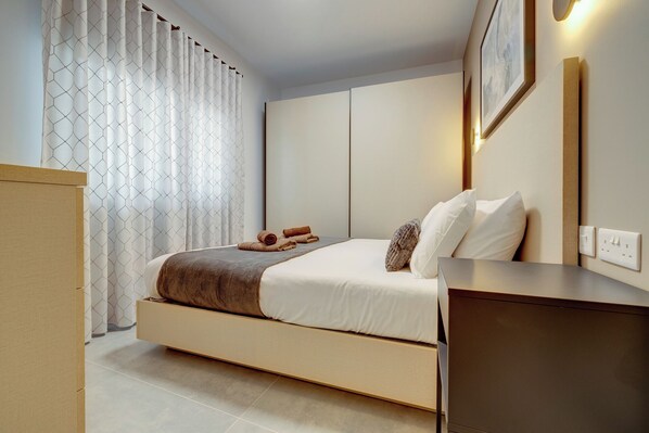 A modern hotel room with a bed, a bedside table, a wall-mounted light, and a curtain with a geometric pattern.