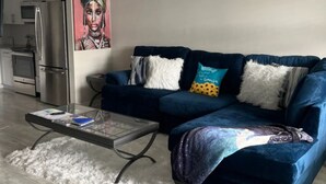 A modern living room with a blue sofa, a glass coffee table, and a ceiling fan.