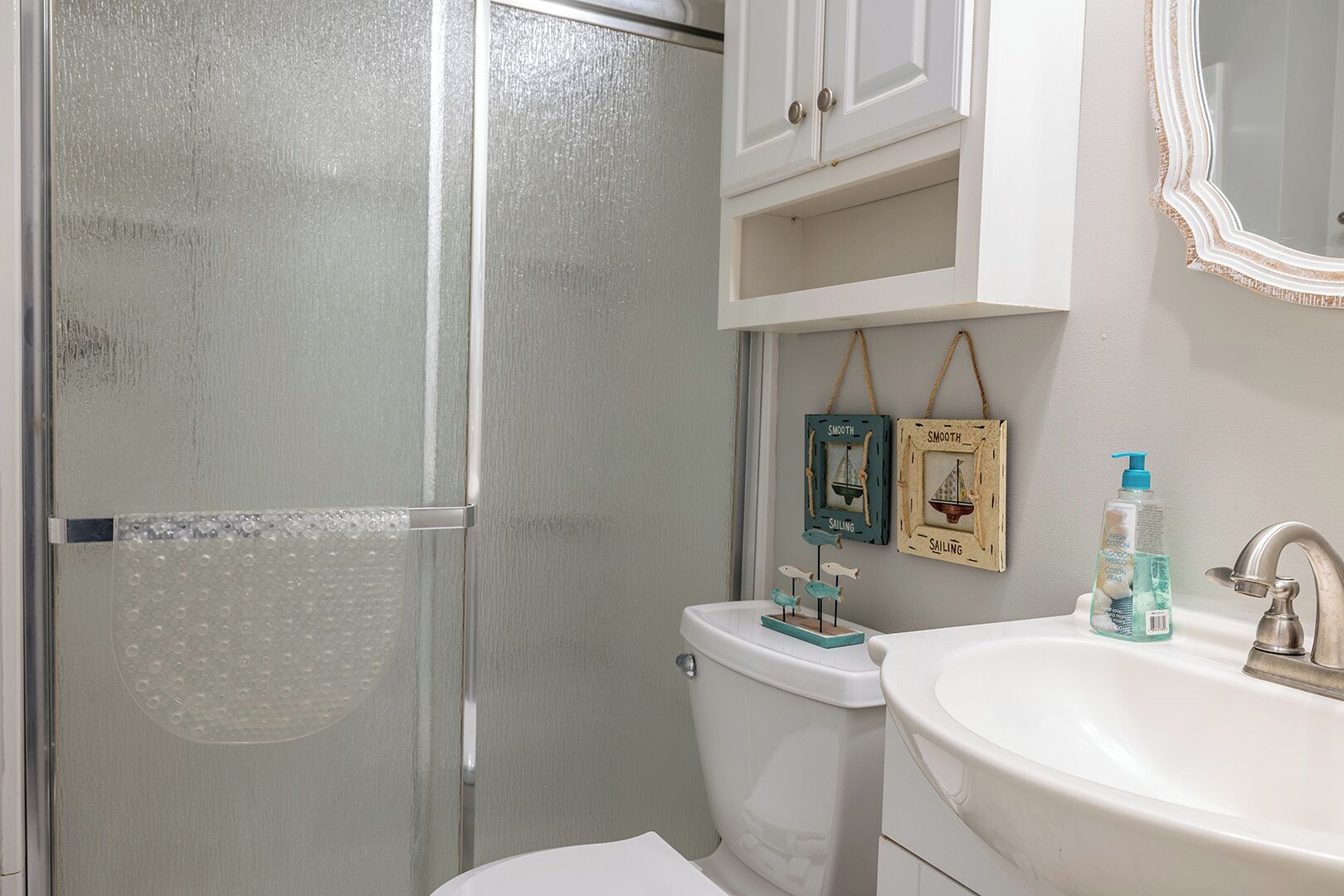 A bathroom with a glass shower enclosure, a toilet, a sink with a mirror, and decorative items on the wall.