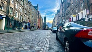 A cobblestone street lined with historic buildings, a parked car, and a distant church spire. - Cozy Edinburgh Apartment Escape (Edinburgh)