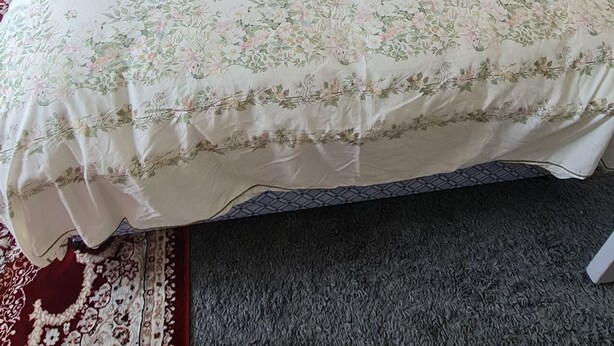 Una cama bien hecha con colcha floral, cabecera de madera y mesita de noche con lámpara.