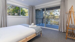 A bedroom with a bed, a wooden ladder, and a balcony with a view of trees.
