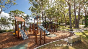 Ein Spielplatz mit Rutsche, Klettergerüsten und Picknickplatz in der Nähe von Wasser.