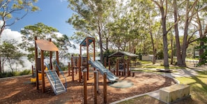 A playground with a slide, climbing structures, and a picnic area near a body of water. - Billie's on Smiths- Lakefront holiday home (Smiths Lake)