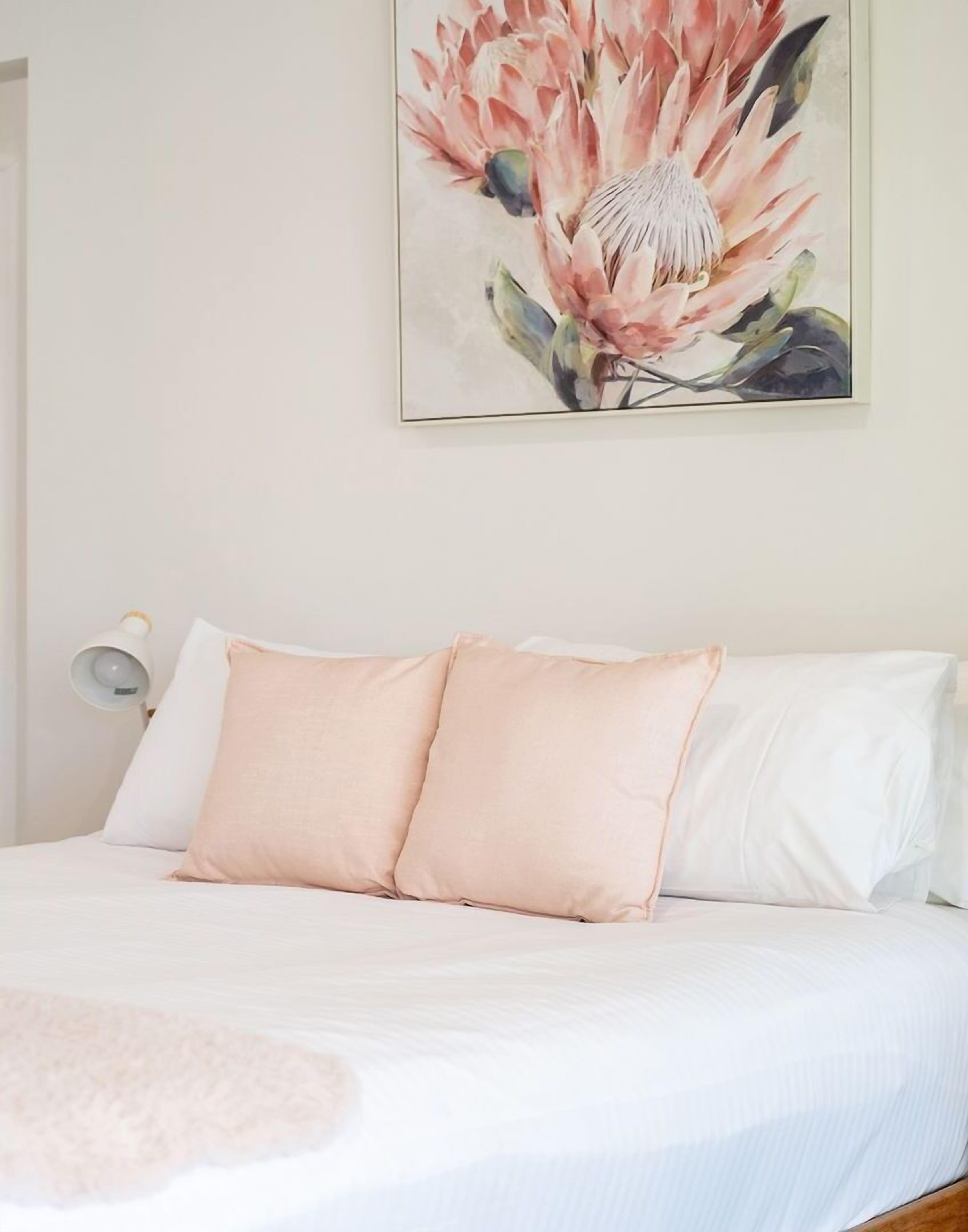 A bedroom with a bed, two pillows, a bedside lamp, and a wall-mounted painting.