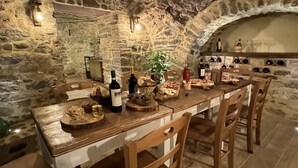 Un espace de restauration aux murs de pierre, avec une longue table en bois dressée pour un repas, où l'on peut voir divers plats et des bouteilles de vin.