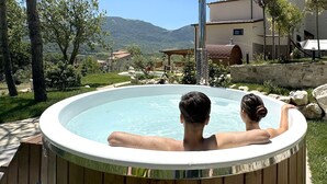 Un bain à remous où se trouvent deux personnes, entouré d’une terrasse en bois, avec une vue sur les montagnes en arrière-plan.