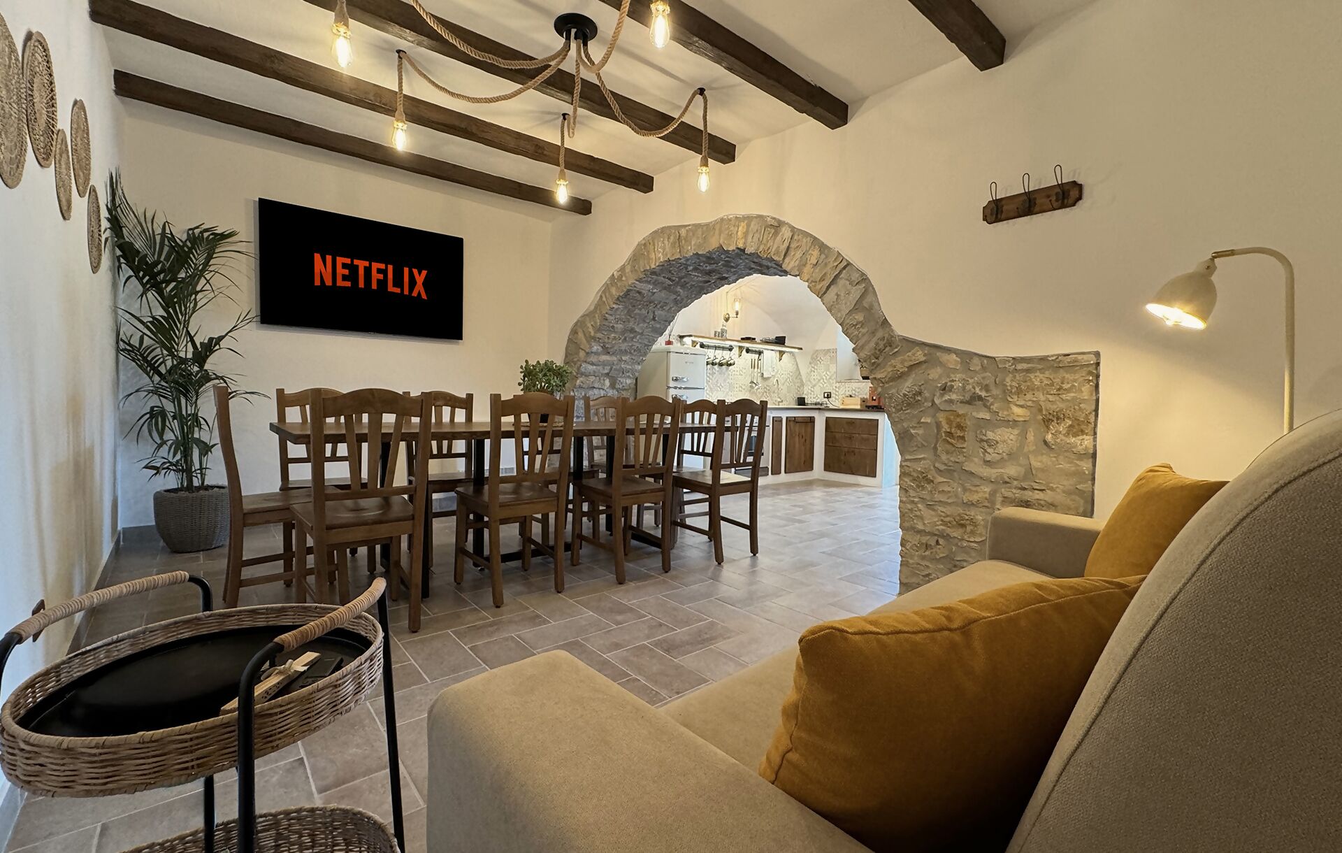 A cozy living room with a stone archway, wooden furniture, and a Netflix sign on the wall.