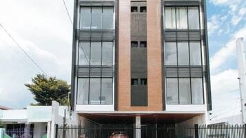 A modern building with a central entrance, large windows, and a metal fence in front.
