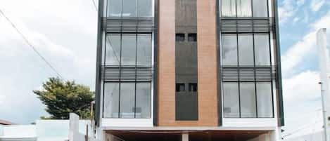 Um edifício moderno com entrada central, janelas amplas e grade de metal na frente.