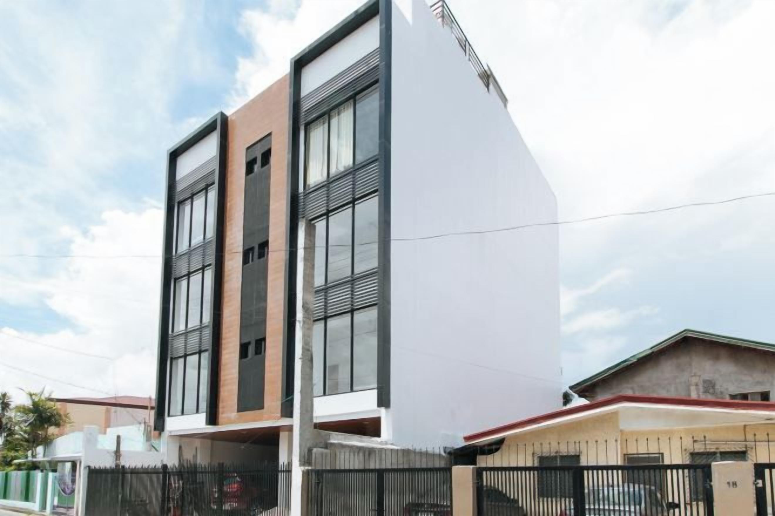 A modern building with a flat roof, large windows, and a visible balcony.