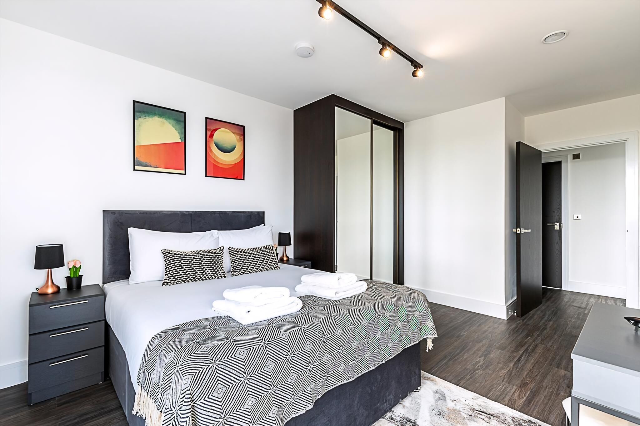 A modern bedroom with a large bed, a nightstand, a mirror, and artwork on the wall.