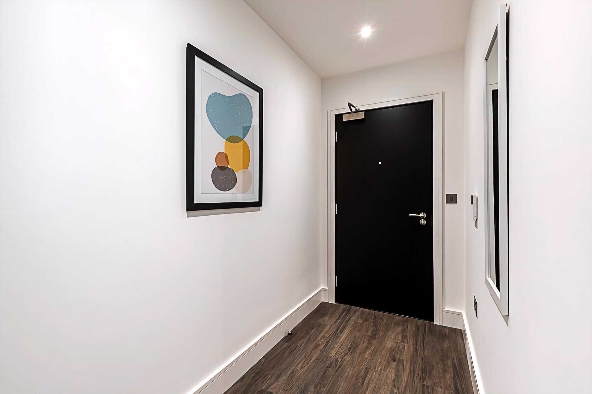 Un corridoio con una porta nera, un quadro astratto incorniciato e un pavimento in legno.