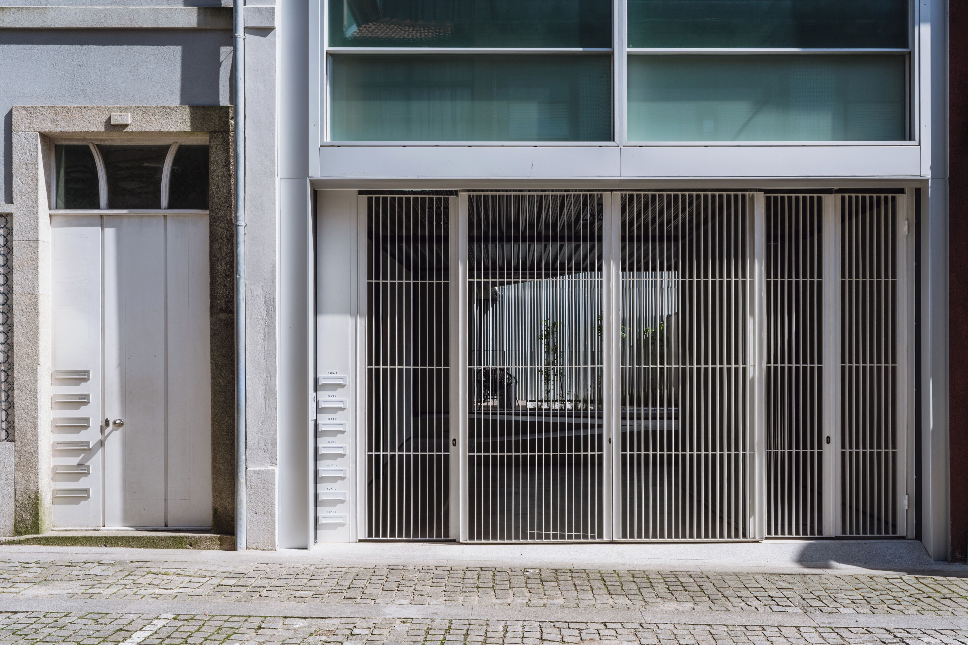 Um edifício com um grande portão de metal, uma porta branca e uma área de entrada pavimentada.