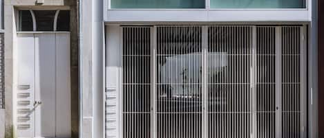 Un edificio con un gran portón metálico, una puerta blanca y un acceso pavimentado.