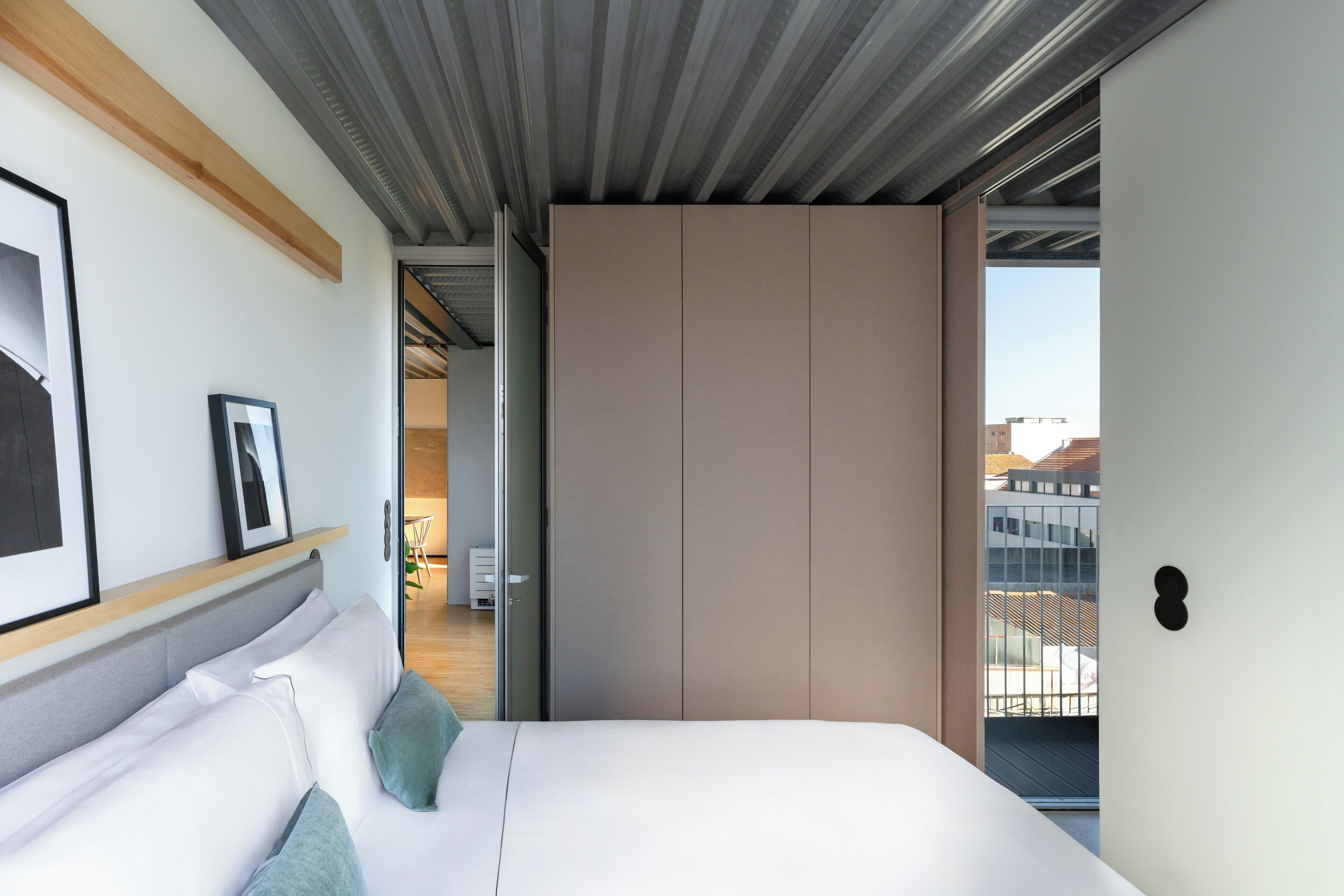 A modern bedroom with a large bed, a wardrobe, and a balcony with a city view.
