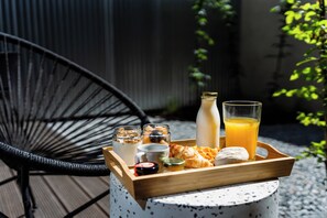 Ontbijtbakje met croissants, een fles melk, een glas jus d'orange en diverse toevoegingen op een buitentafel.