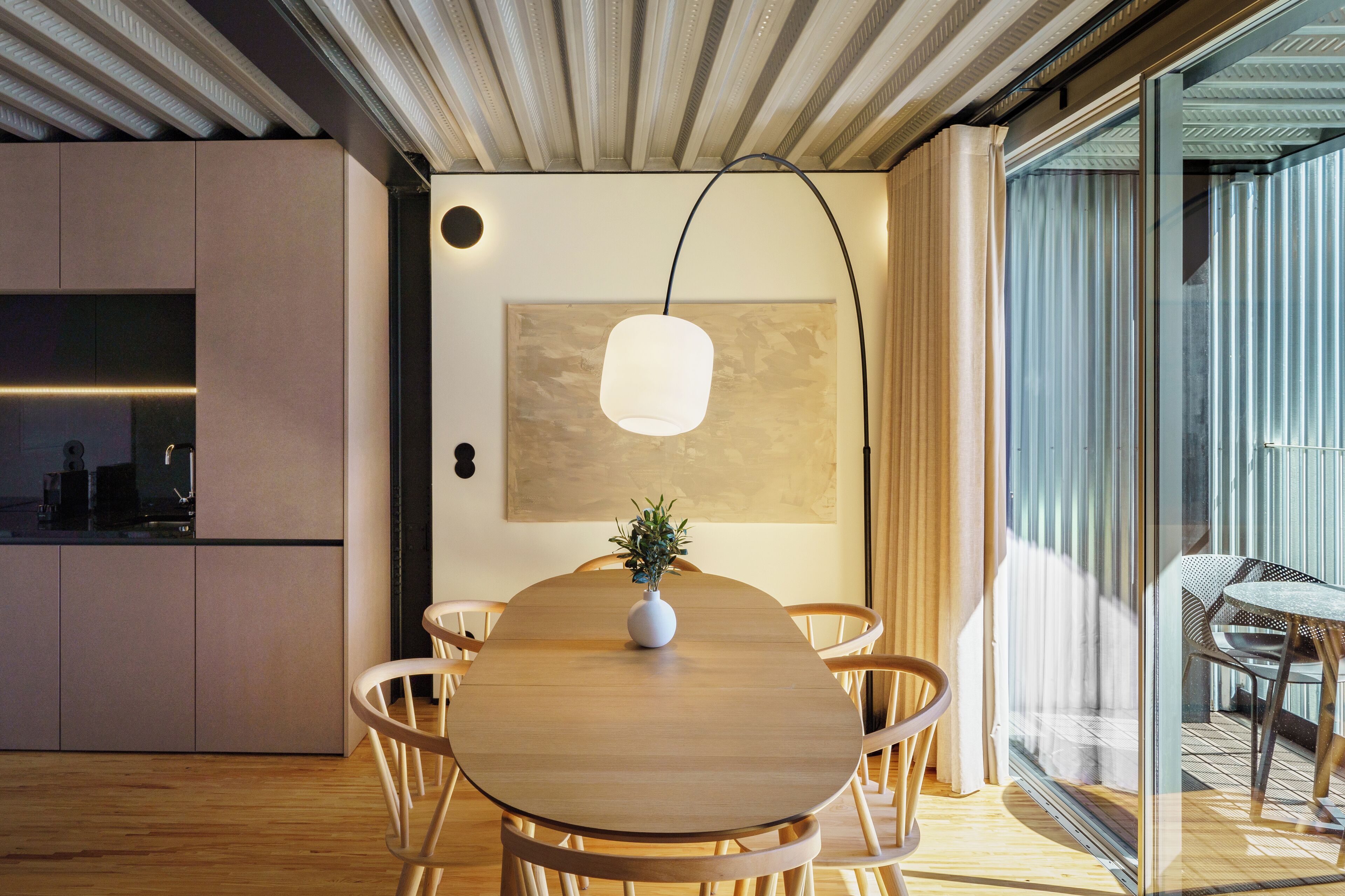 A modern dining area with a wooden table, chairs, a vase with a plant, and a pendant light.