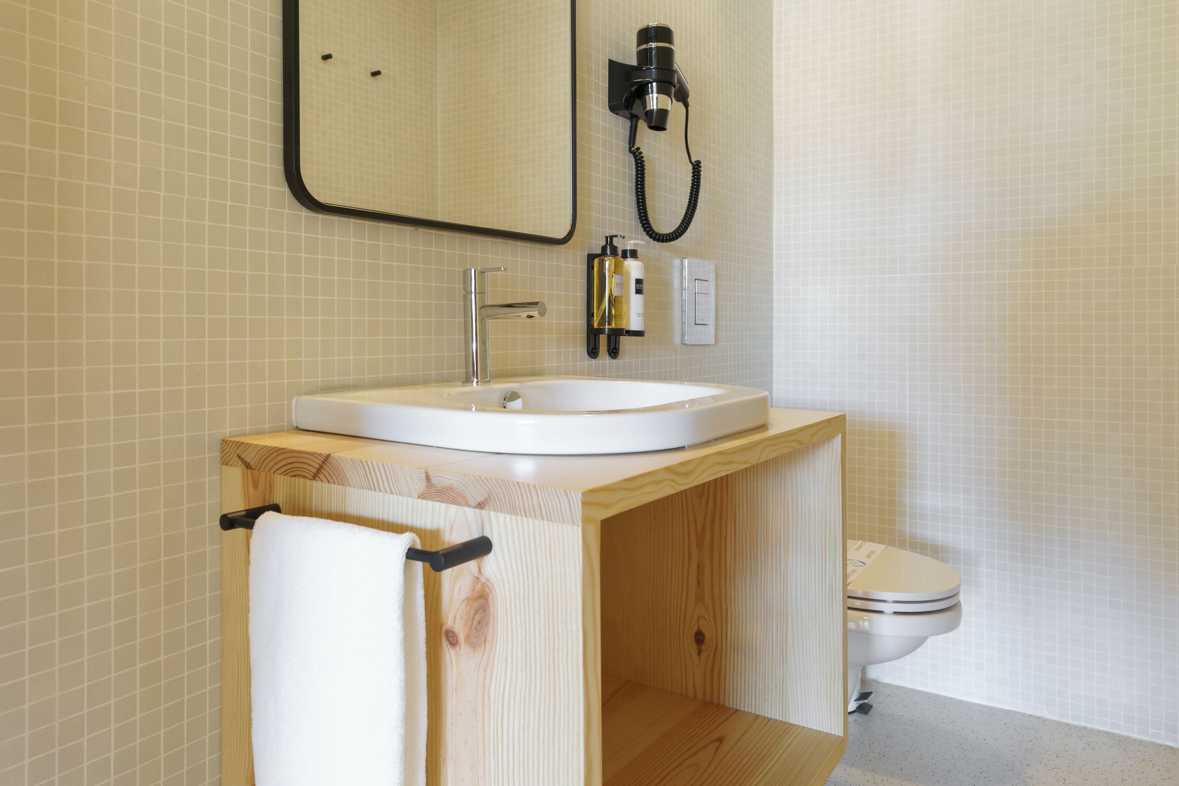 A bathroom with a wooden vanity, a white sink, a mirror, a hairdryer, and a toilet.