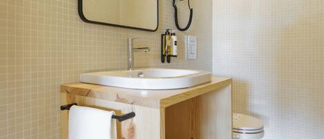 A bathroom with a wooden vanity, a white sink, a mirror, a hairdryer, and a toilet.