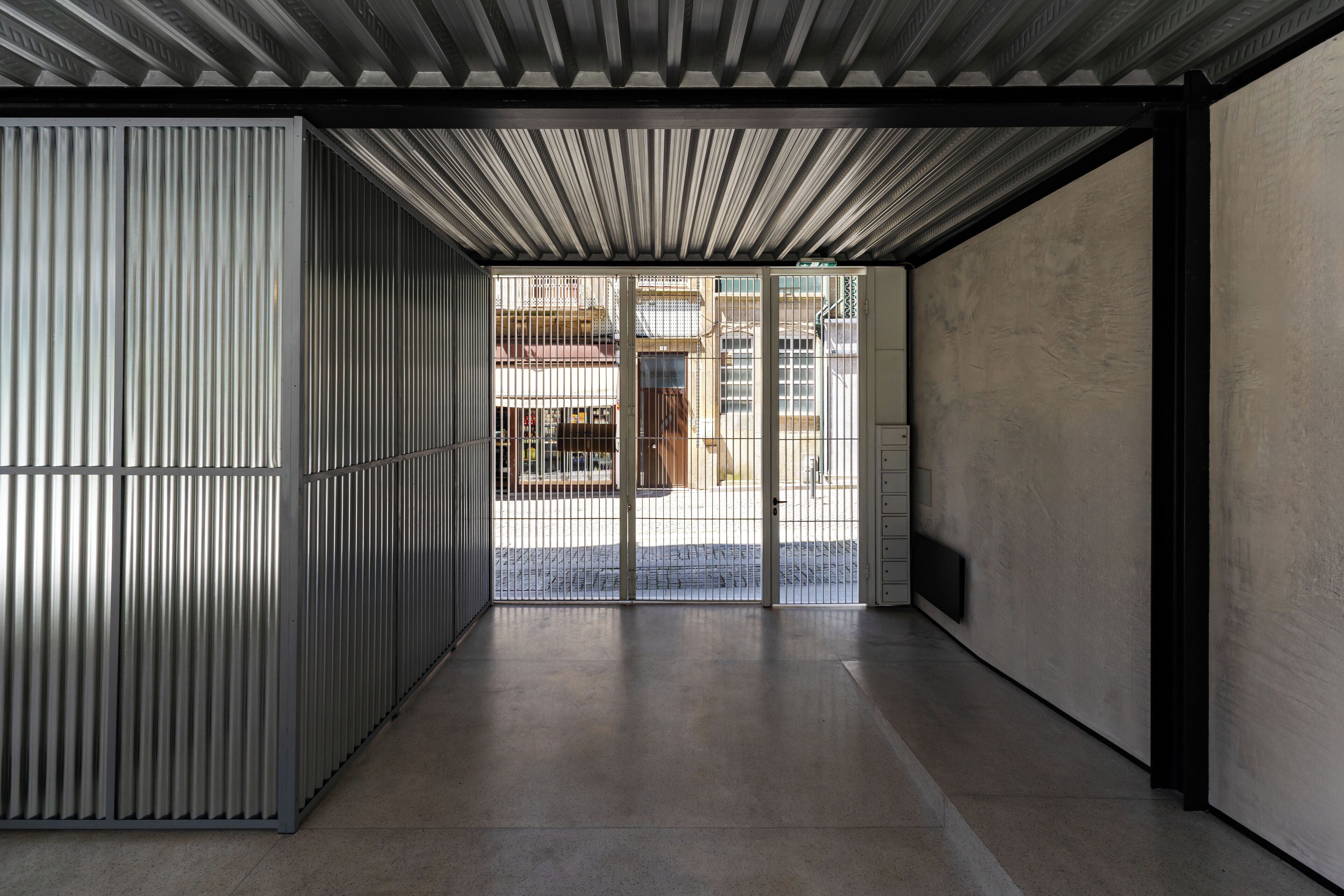 Un interior moderno con pared de metal, suelo de hormigón y vistas al exterior a través de una puerta de cristal.
