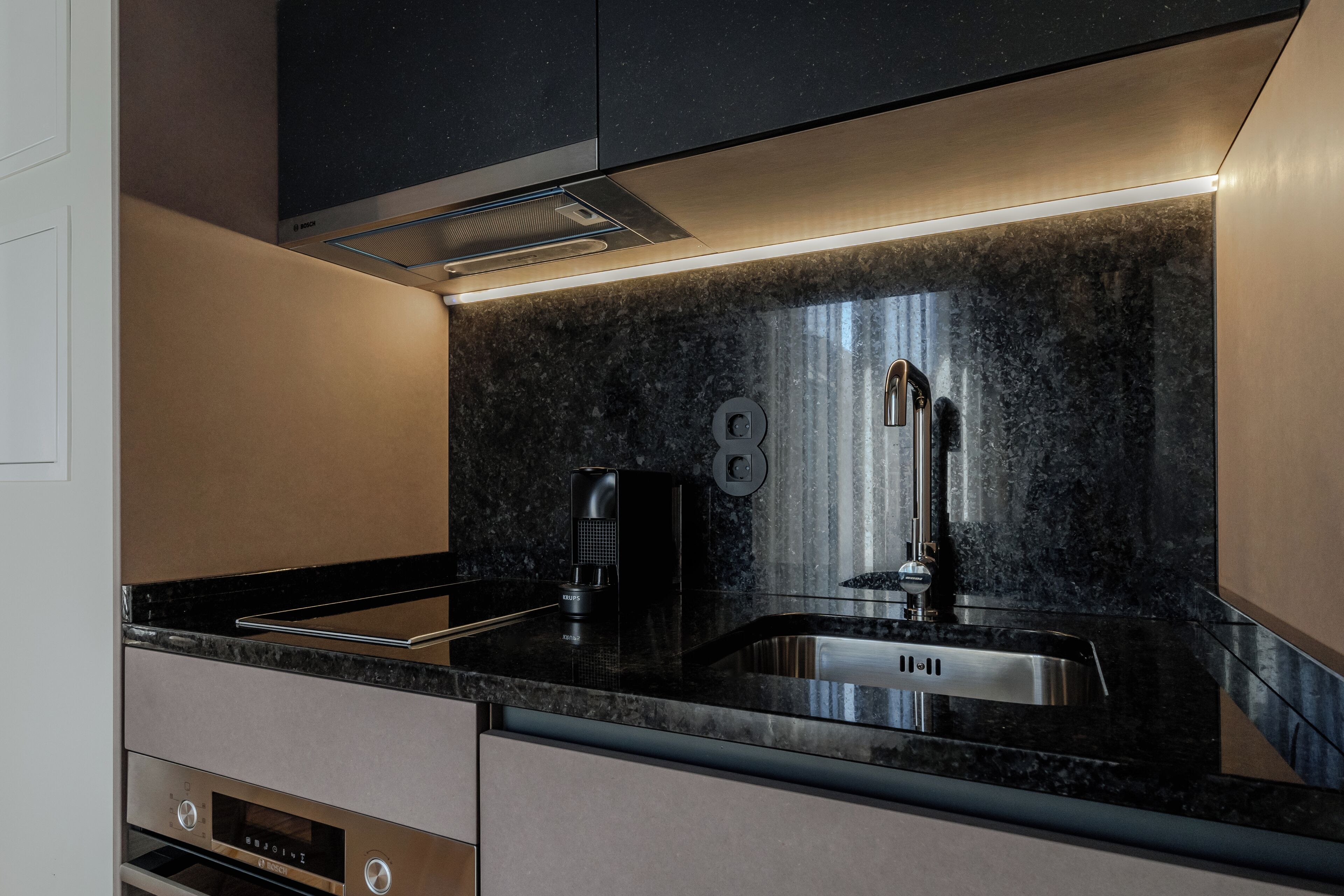 Una cocina moderna con encimera negra, electrodomésticos de acero inoxidable y horno empotrado.