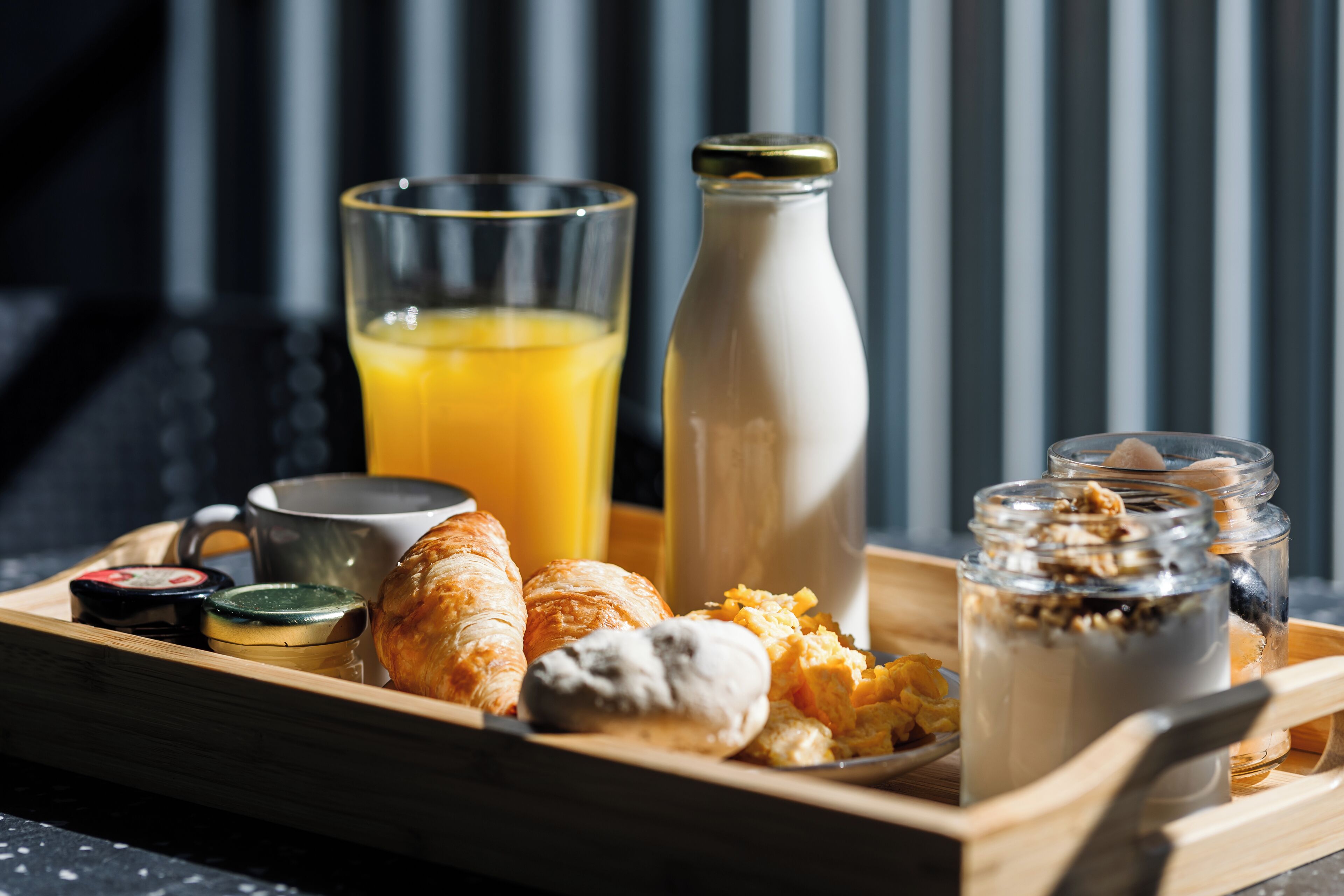 A breakfast tray with croissants, orange juice, a bottle of milk, and jars of yogurt and granola.
