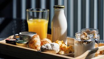 A breakfast tray with croissants, orange juice, a bottle of milk, and jars of yogurt and granola.