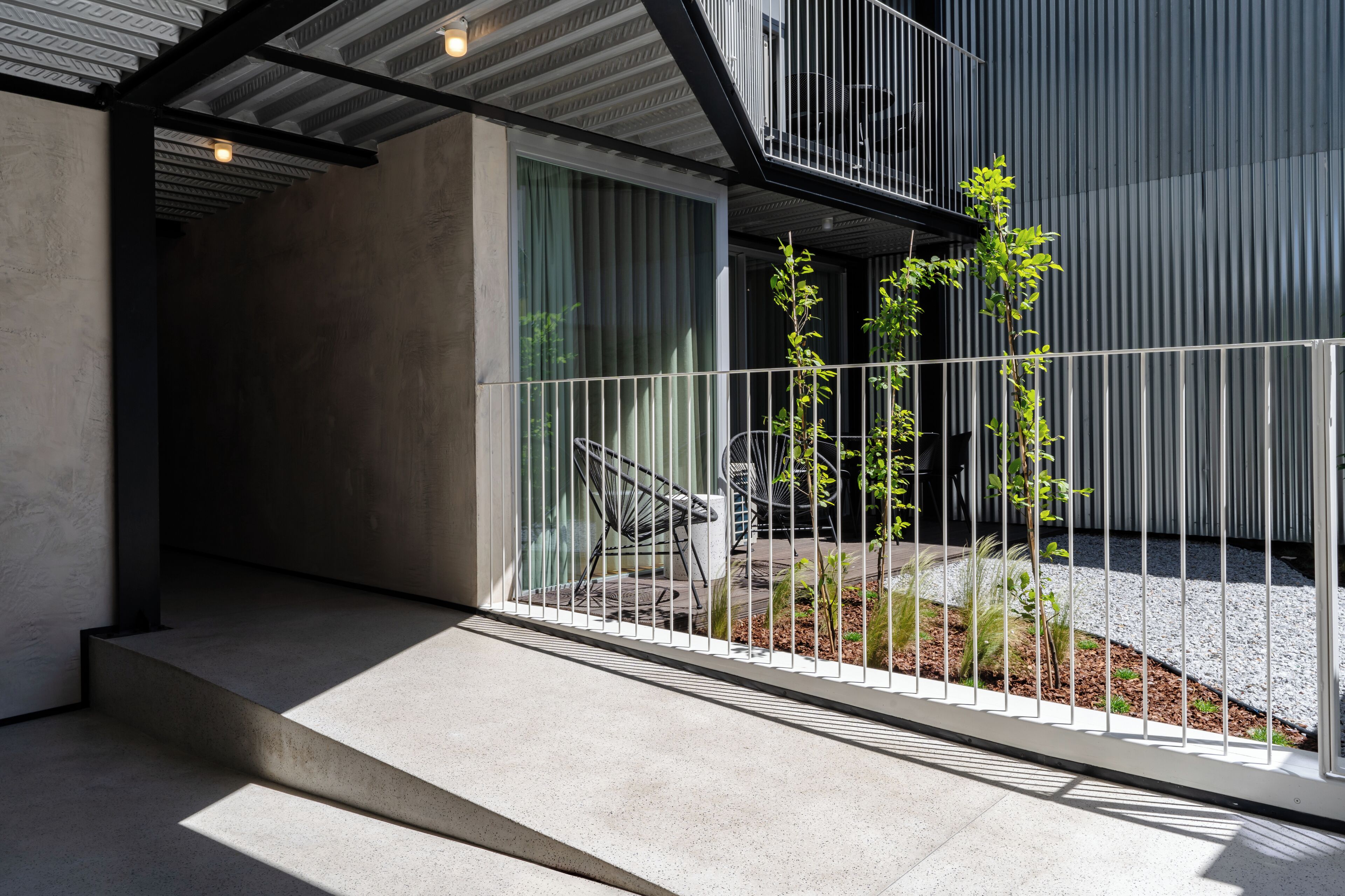 A modern outdoor area with a concrete floor, metal railing, and a small garden with young plants.
