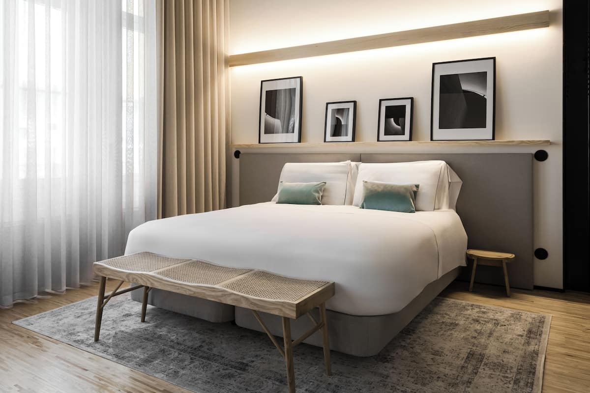 Une chambre moderne avec un grand lit, une petite table de chevet, un banc et une étagère murale décorée de tableaux encadrés.