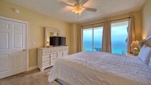 Ein Schlafzimmer mit Bett, Schminktisch, Fernseher, Deckenventilator und Blick auf den Ozean.