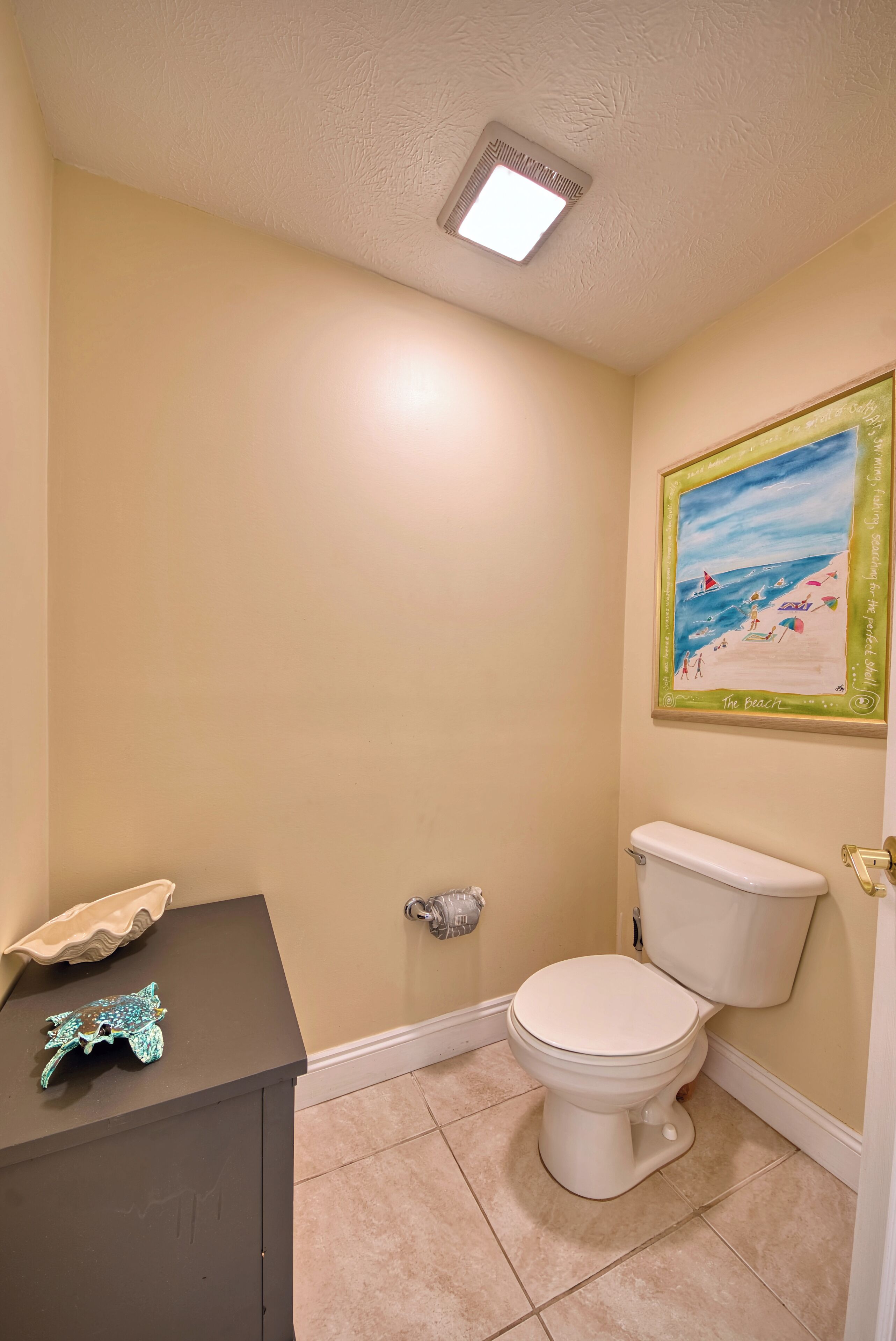 A bathroom with a toilet, a sink with decorative items, and a beach-themed wall art.