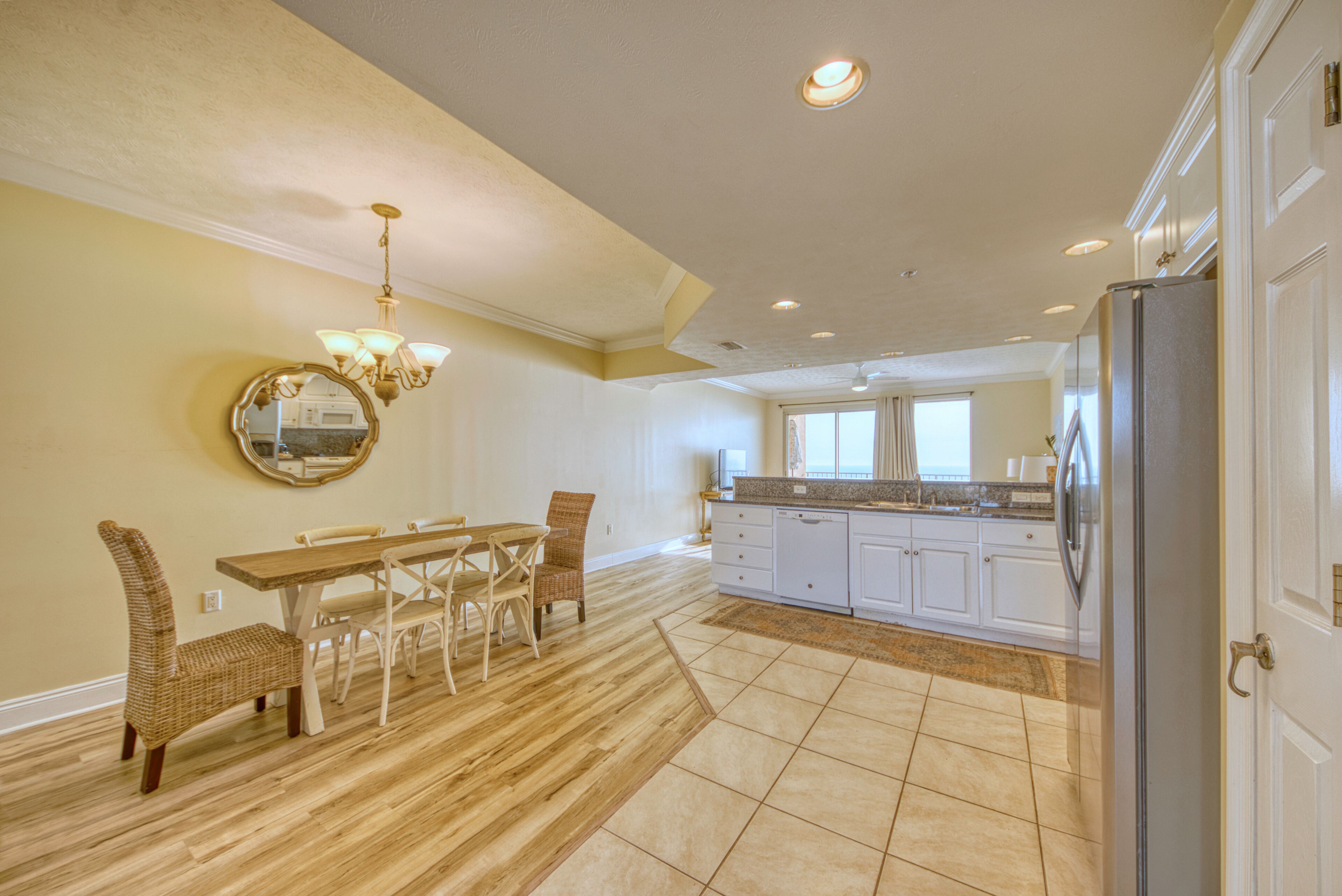 A spacious kitchen with white cabinets, a dining area with a wooden table and wicker chairs, and a large mirror on the wall.
