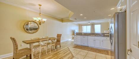 A spacious kitchen with white cabinets, a dining area with a wooden table and wicker chairs, and a large mirror on the wall.