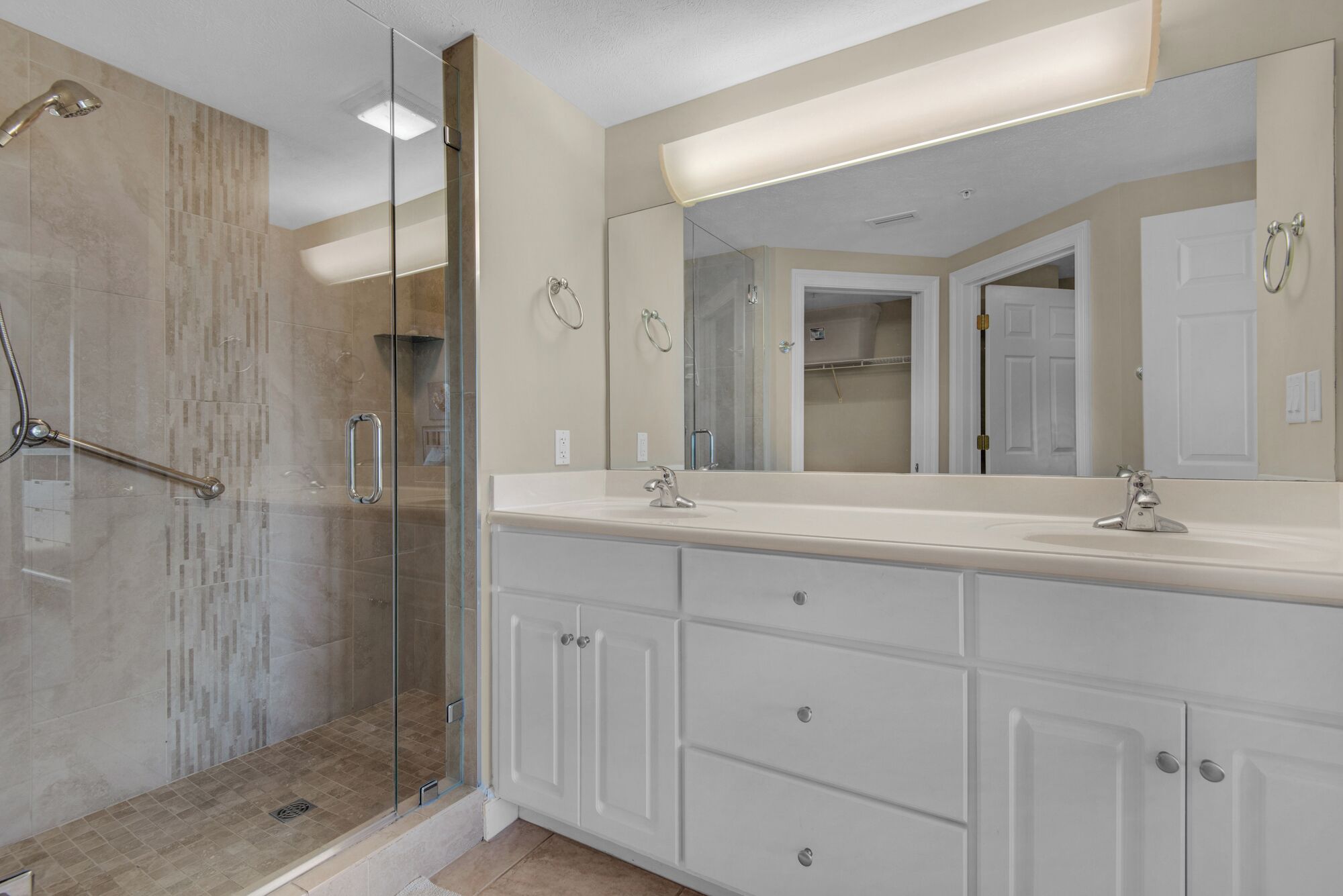 A modern bathroom with a glass shower enclosure, a large vanity with a mirror, and a walk-in closet.