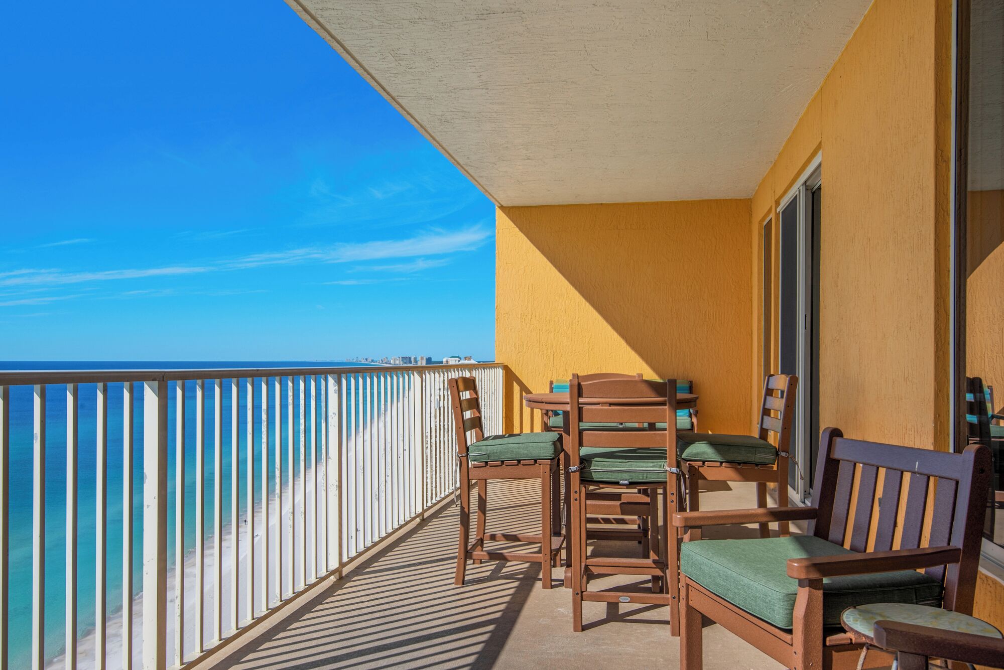A balcony with a view of the ocean, wooden chairs, and a table.