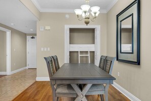 A dining room with a long table, chairs, a chandelier, and a large mirror on the wall. - Treasure Island 1911 (Panama City Beach)