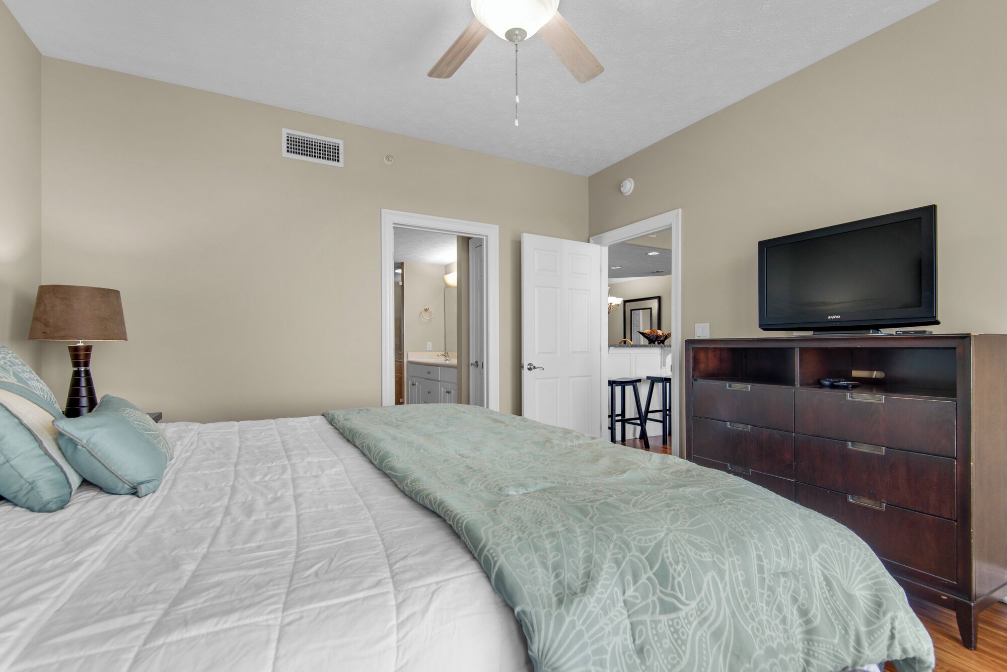 A bedroom with a bed, a TV, a dresser, and a ceiling fan.
