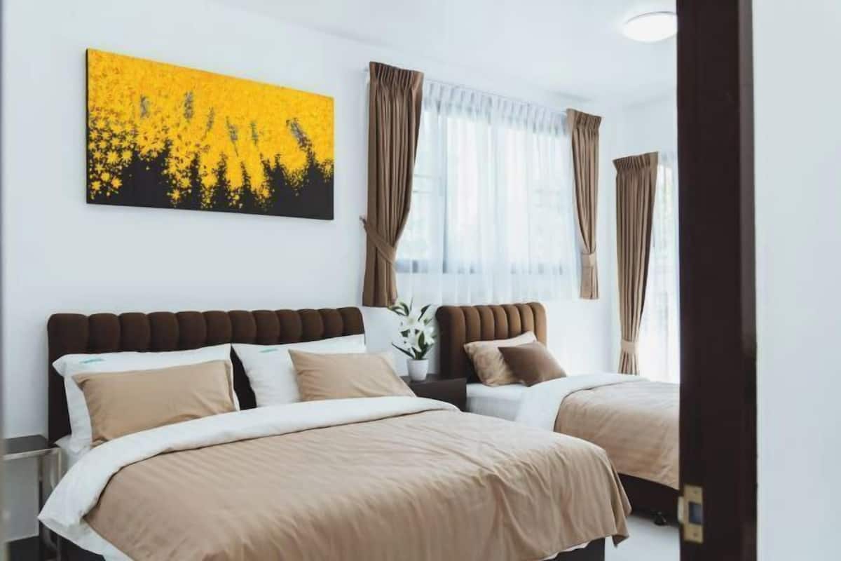 Una camera d'albergo con due letti, una grande finestra con tende, un quadro appeso e un comodino con una pianta.