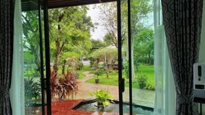 Une vue à travers une porte vitrée d’un jardin avec un sentier, des plantes en pot et un petit élément décoratif aquatique.