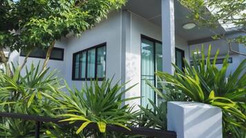A modern building with large windows, a white facade, and lush green plants in the foreground.