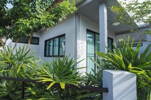 Un edificio moderno con amplios ventanales, fachada blanca y exuberante vegetación en primer plano.